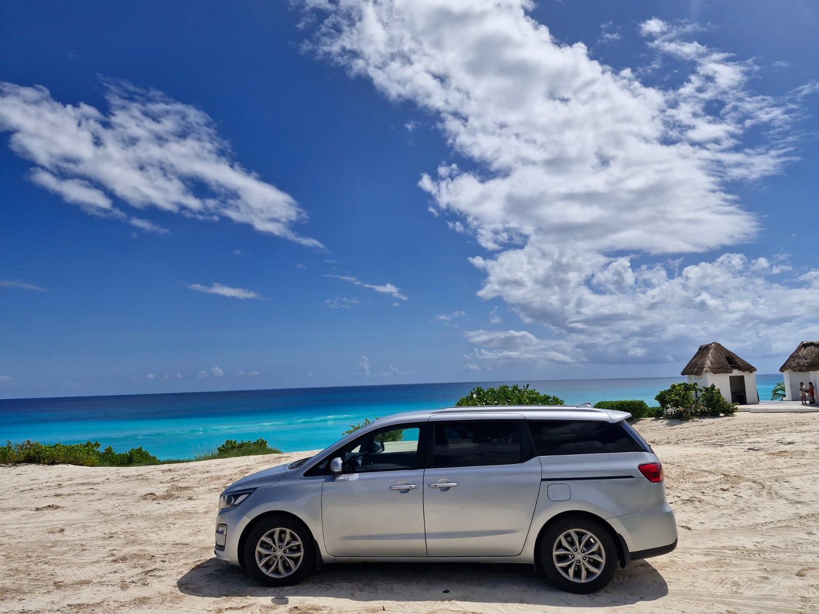 White premium transfer van parked near the Cancun coastline for private airport transportation.